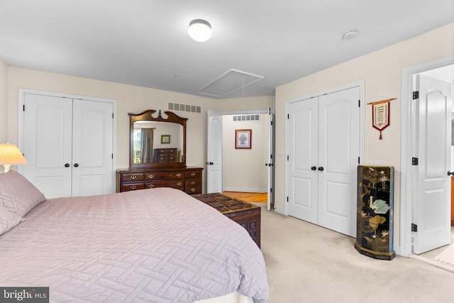 bedroom with visible vents, light carpet, two closets, and attic access