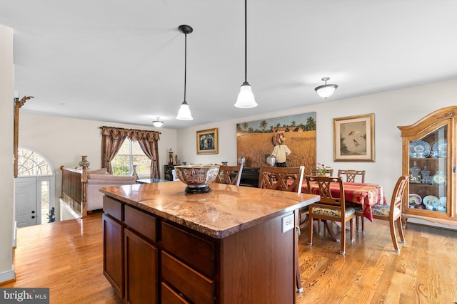 kitchen with hanging light fixtures, light stone counters, light wood finished floors, and a center island