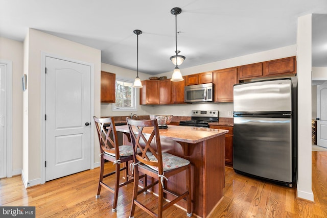 kitchen with decorative light fixtures, light wood-style flooring, stainless steel appliances, and a kitchen bar