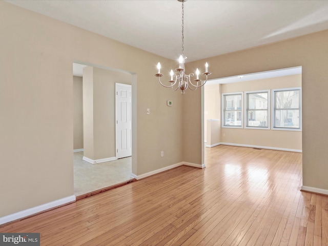 unfurnished dining area with a notable chandelier, baseboards, and light wood-style floors