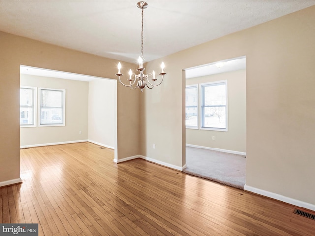 unfurnished room featuring hardwood / wood-style floors, an inviting chandelier, baseboards, and visible vents