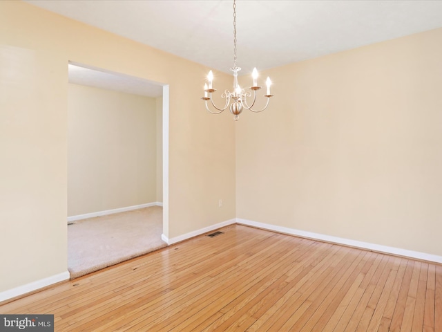 empty room with hardwood / wood-style floors, an inviting chandelier, baseboards, and visible vents