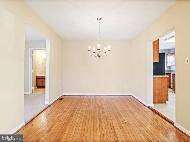 unfurnished dining area featuring a chandelier, baseboards, and light wood-style flooring