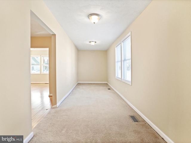 carpeted spare room with a wealth of natural light, visible vents, and baseboards