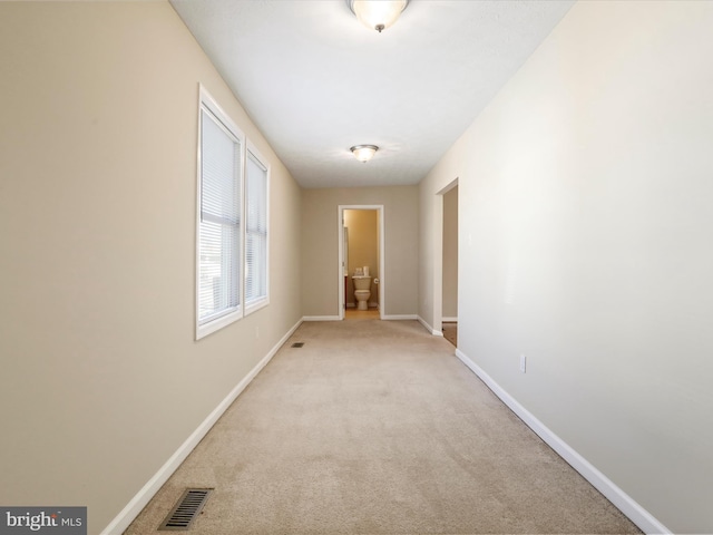 hall with light colored carpet, visible vents, and baseboards