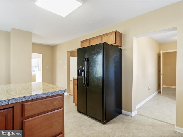 kitchen with light countertops, baseboards, brown cabinets, and black refrigerator with ice dispenser