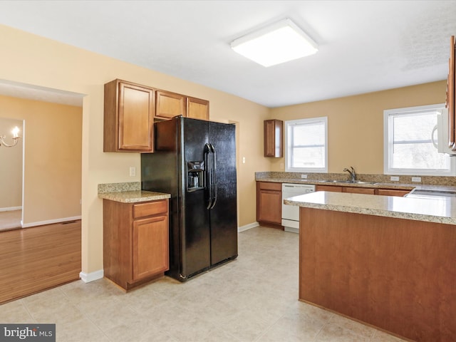 kitchen featuring brown cabinets, a sink, light countertops, dishwasher, and black refrigerator with ice dispenser