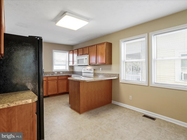 kitchen featuring visible vents, white appliances, a peninsula, brown cabinetry, and baseboards