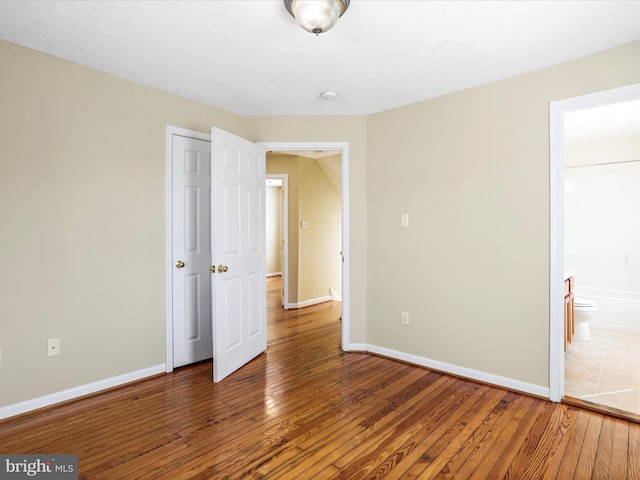 unfurnished bedroom featuring ensuite bathroom, baseboards, and hardwood / wood-style floors