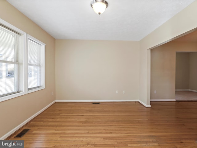 empty room with visible vents, light wood-type flooring, and baseboards