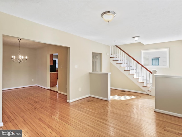 unfurnished living room featuring a chandelier, light wood-style flooring, stairs, and baseboards