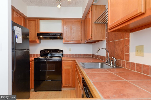 kitchen featuring black appliances, tile counters, under cabinet range hood, and a sink