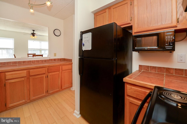 kitchen with black appliances, a textured ceiling, tile countertops, light wood-style floors, and ceiling fan