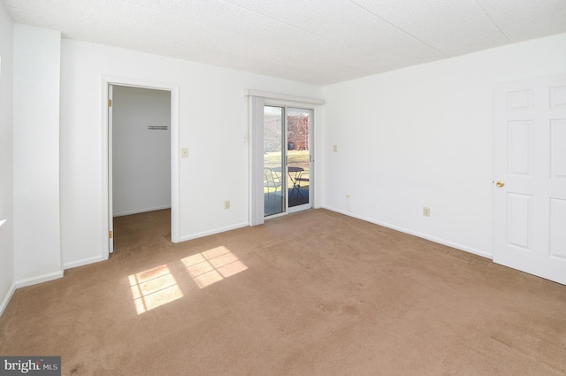 unfurnished bedroom featuring access to exterior, carpet flooring, a walk in closet, and baseboards