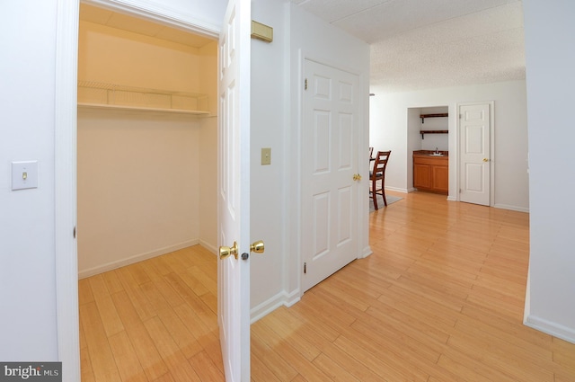 hall with light wood-style flooring, baseboards, and a textured ceiling