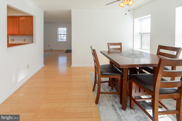 dining space with light wood-style flooring, a textured ceiling, baseboards, and a ceiling fan