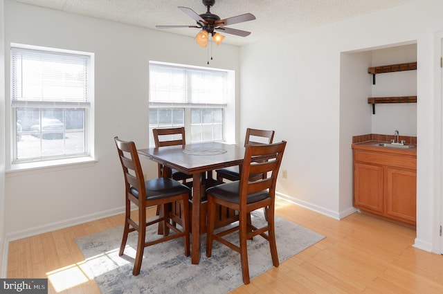 dining space with wet bar, a textured ceiling, a ceiling fan, and light wood finished floors