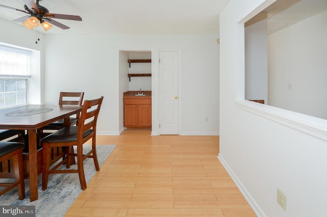 dining space featuring light wood-style flooring, a textured ceiling, baseboards, and a ceiling fan