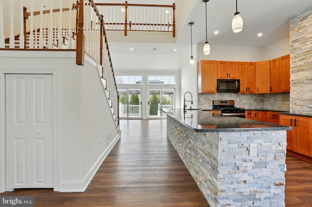 kitchen featuring stainless steel gas range oven, a sink, dark wood finished floors, a high ceiling, and black microwave