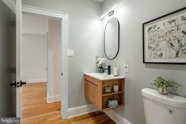 bathroom with toilet, vanity, baseboards, and wood finished floors