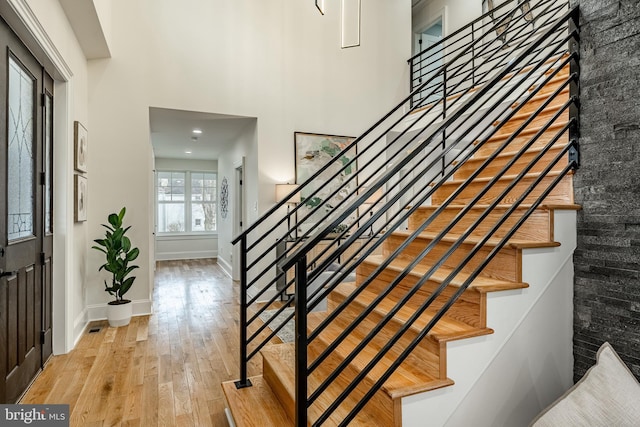 interior space featuring stairway, light wood-type flooring, baseboards, and a towering ceiling