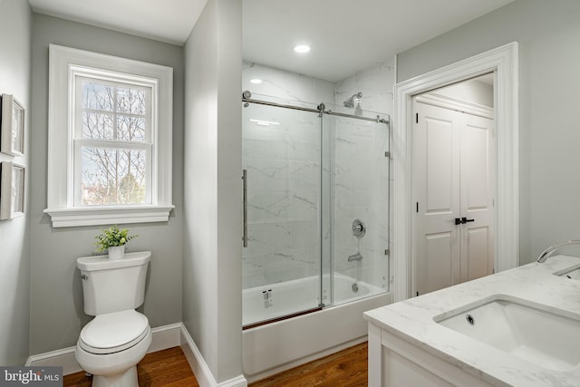 bathroom with baseboards, toilet, wood finished floors, combined bath / shower with glass door, and a sink