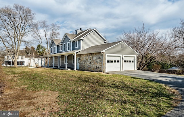 view of front of home with an attached garage, a shingled roof, a front lawn, stone siding, and driveway