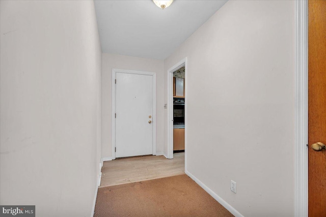 corridor featuring light colored carpet and baseboards