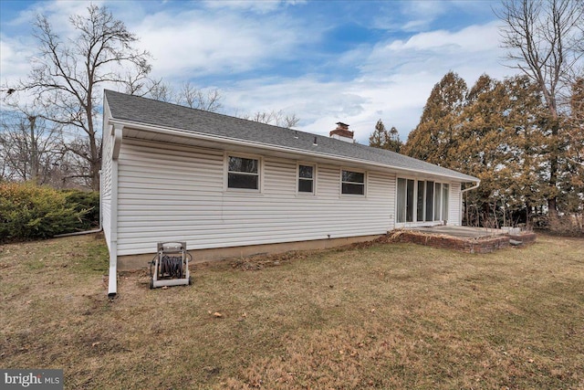 back of property featuring a lawn, a chimney, a patio, and roof with shingles