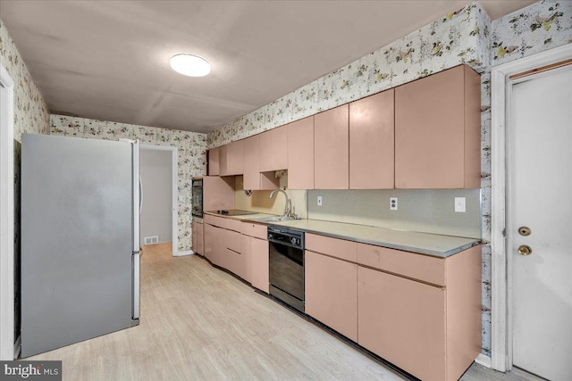 kitchen with light wood finished floors, wallpapered walls, light countertops, black appliances, and a sink