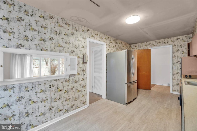 kitchen featuring wallpapered walls, baseboards, light wood-type flooring, freestanding refrigerator, and a sink