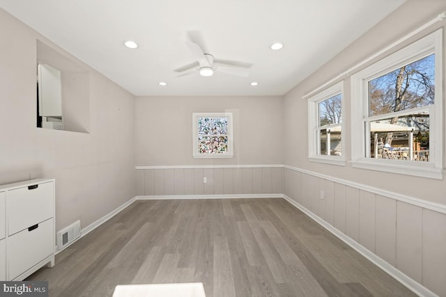 empty room with light wood-type flooring, visible vents, recessed lighting, wainscoting, and ceiling fan