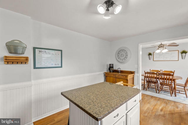 kitchen featuring a ceiling fan, a kitchen island, stone countertops, wainscoting, and light wood-type flooring