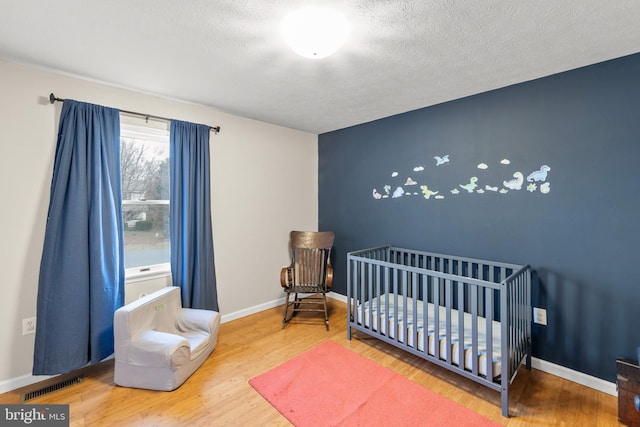 bedroom with visible vents, baseboards, wood finished floors, a textured ceiling, and a nursery area