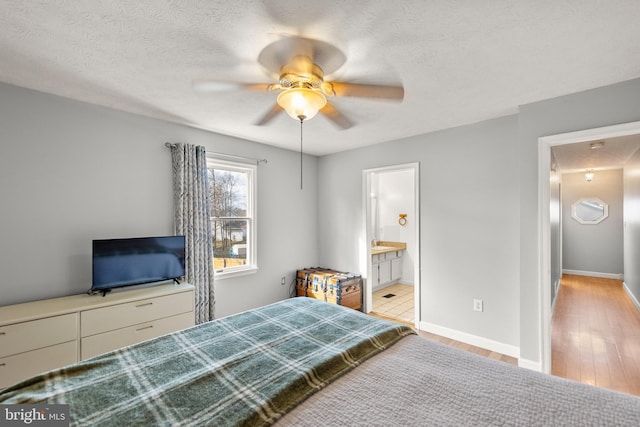 bedroom featuring light wood-type flooring, ensuite bathroom, a ceiling fan, a textured ceiling, and baseboards