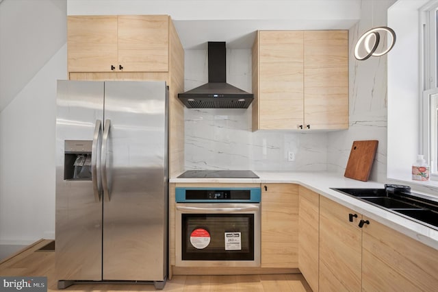 kitchen with light countertops, backsplash, appliances with stainless steel finishes, light brown cabinets, and wall chimney range hood