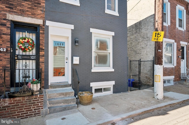 view of exterior entry featuring fence and brick siding