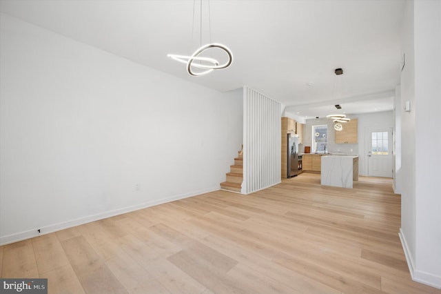 unfurnished living room featuring a chandelier, light wood-style flooring, and baseboards