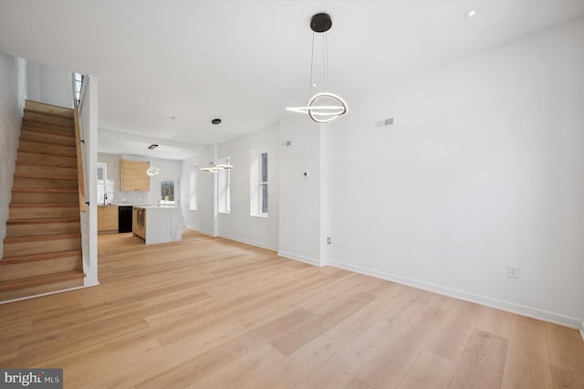 unfurnished living room with baseboards, stairs, and light wood-style flooring