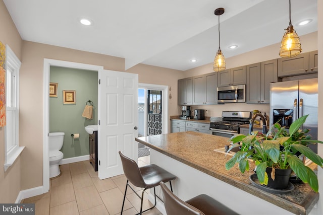 kitchen featuring decorative light fixtures, stainless steel appliances, a breakfast bar, and gray cabinets