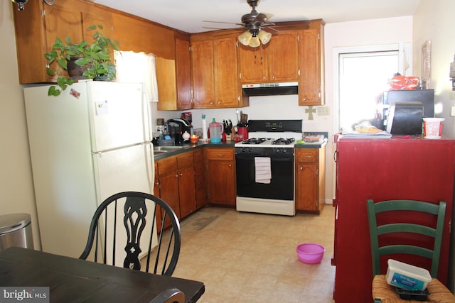 kitchen featuring dark countertops, under cabinet range hood, brown cabinets, freestanding refrigerator, and gas stove