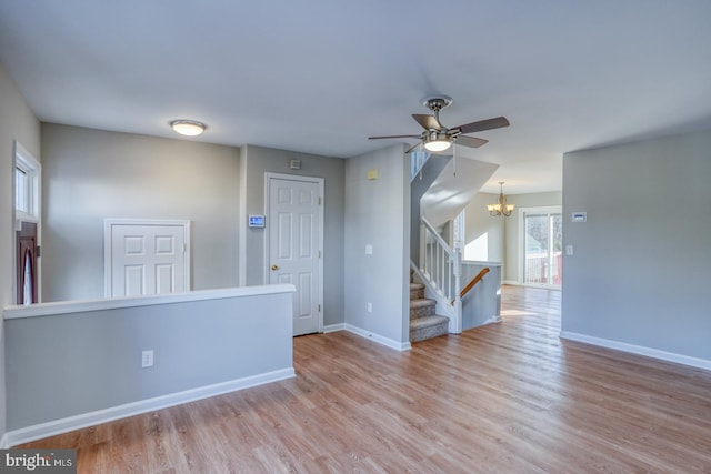 spare room featuring stairway, baseboards, wood finished floors, and ceiling fan with notable chandelier