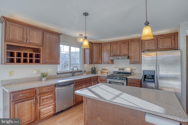 kitchen with a kitchen island, light stone countertops, under cabinet range hood, appliances with stainless steel finishes, and a sink