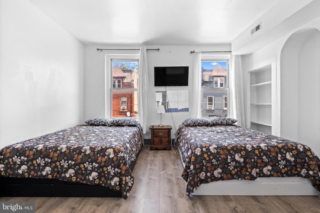 bedroom with visible vents, arched walkways, and wood finished floors