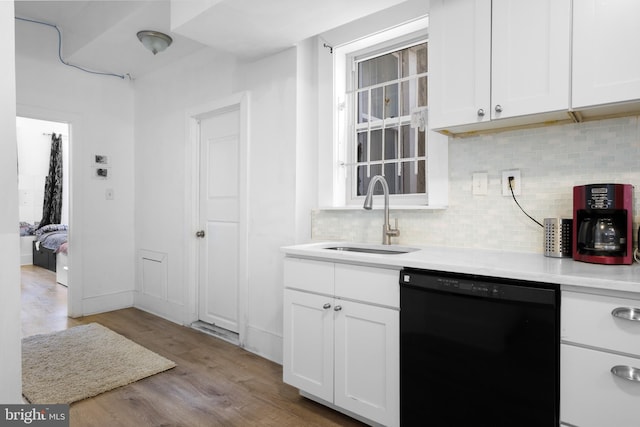 kitchen with white cabinetry, a sink, light wood-style floors, dishwasher, and backsplash