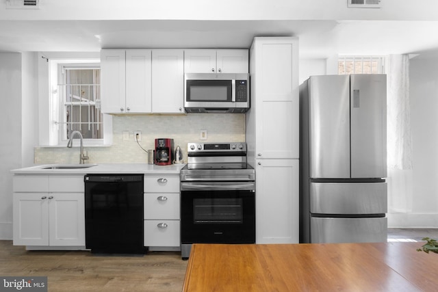 kitchen featuring visible vents, a sink, decorative backsplash, stainless steel appliances, and white cabinetry