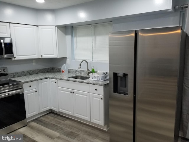 kitchen featuring light stone countertops, wood finished floors, a sink, stainless steel appliances, and white cabinetry