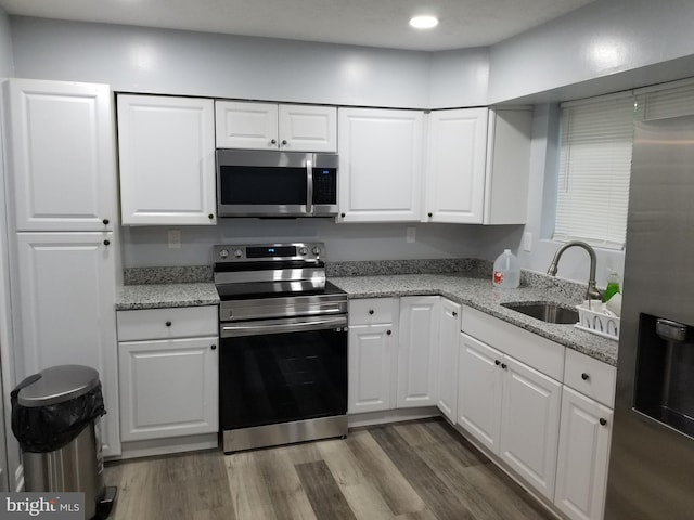 kitchen with light stone countertops, dark wood-style floors, white cabinets, stainless steel appliances, and a sink