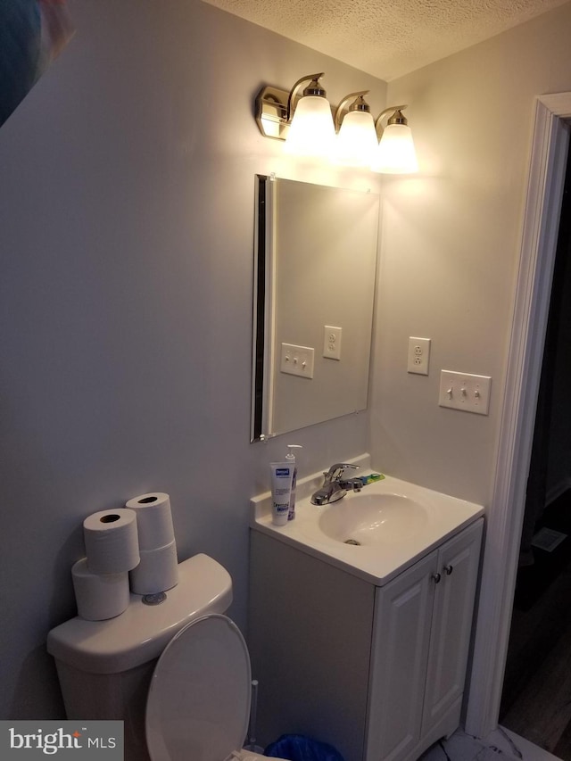 half bathroom featuring vanity, toilet, and a textured ceiling