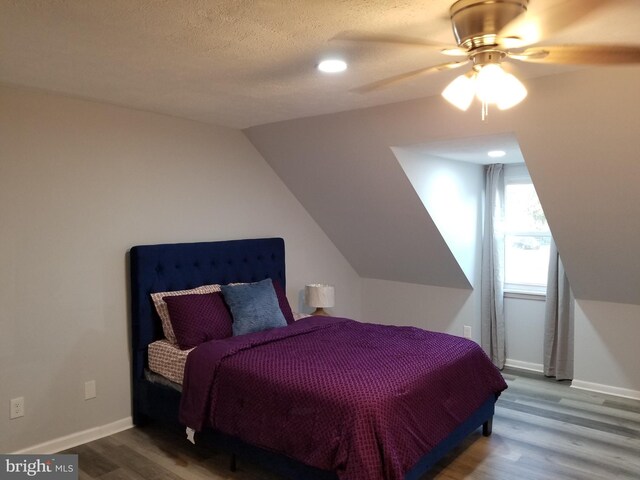 bedroom featuring lofted ceiling, wood finished floors, baseboards, and a textured ceiling